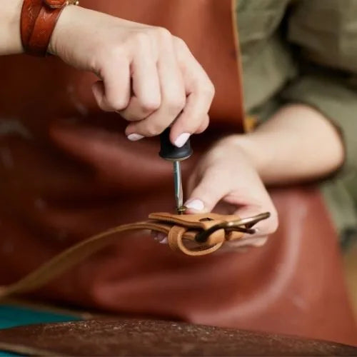 Person fastening a buckle to a leather belt with a screwdriver
