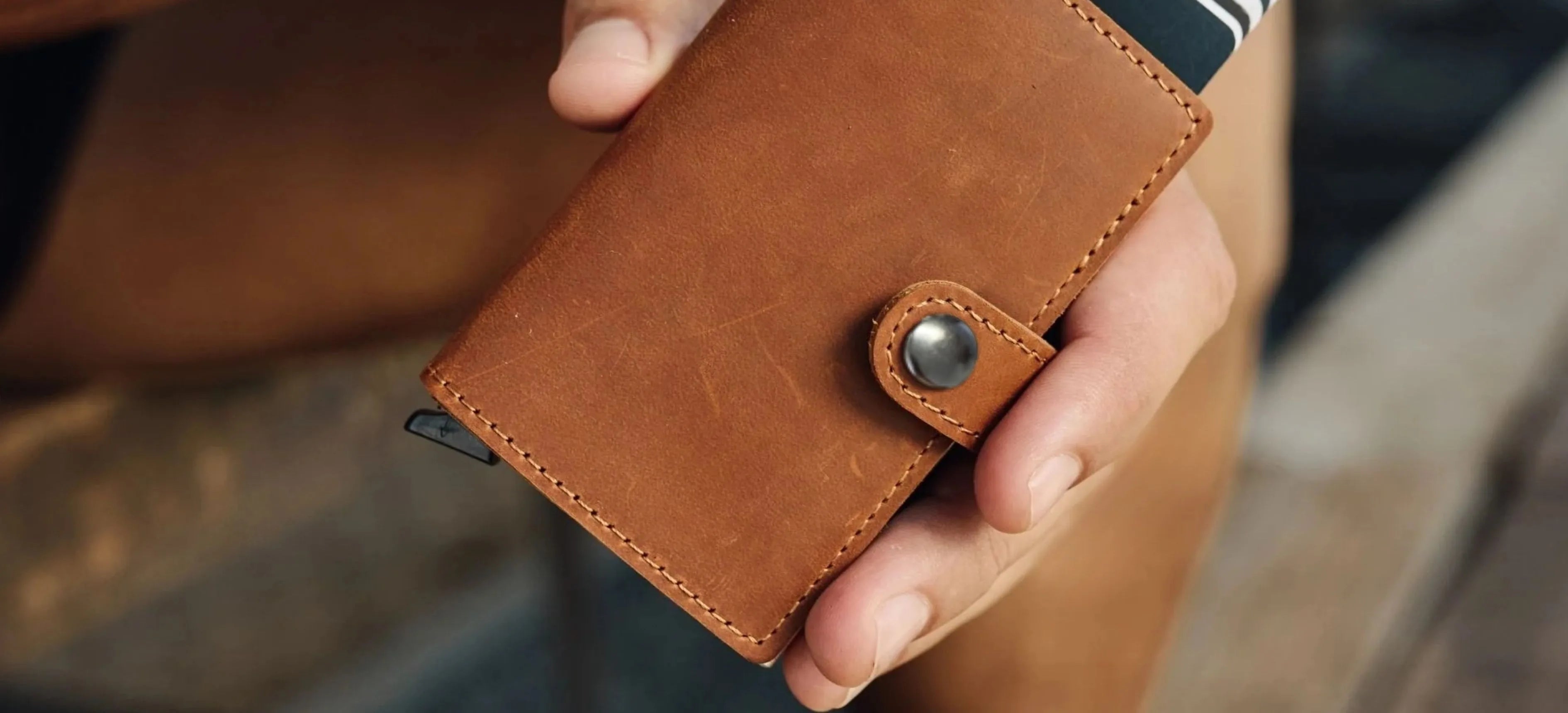 Brown leather wallet held in a hand with a blurred background